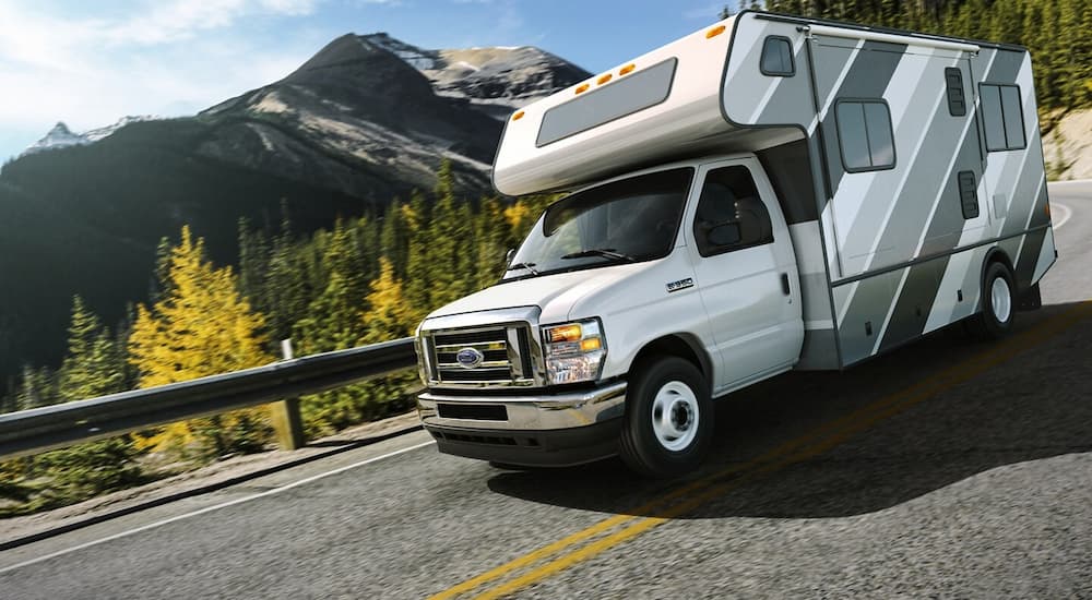 White 2026 Ford E-Series Cutaway with a camper van driving from a dealer with work trucks for sale.