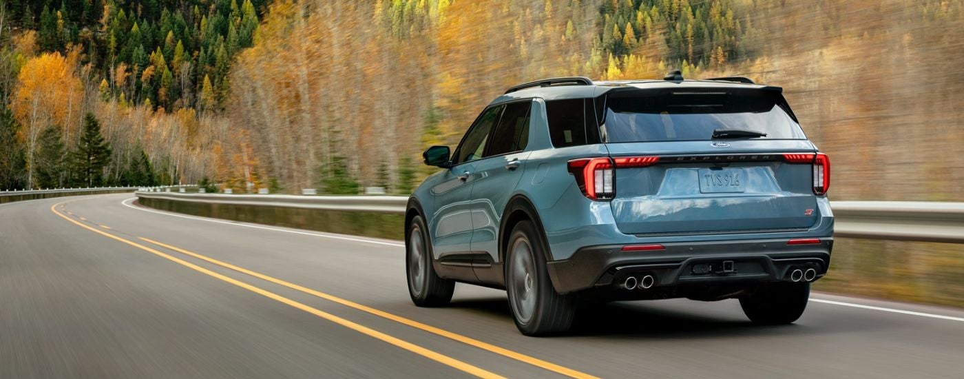 Rear view of a blue 2026 Ford Explorer driving on a paved road.