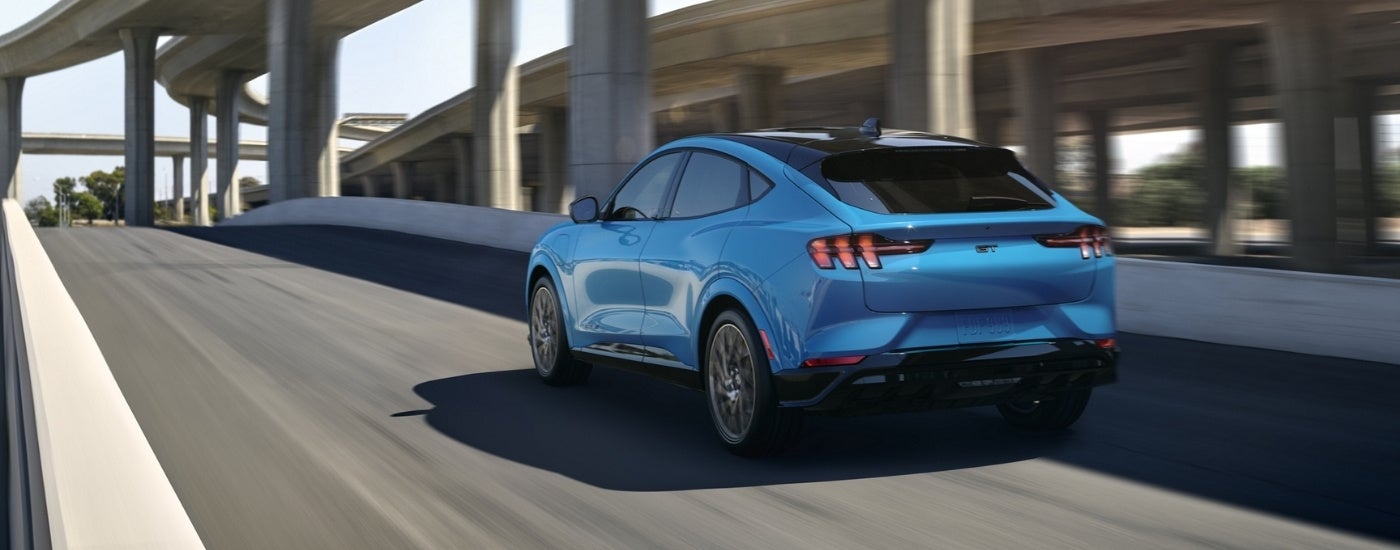A blue 2021 Ford Mustang Mach-E GT driving to a Ford dealer.