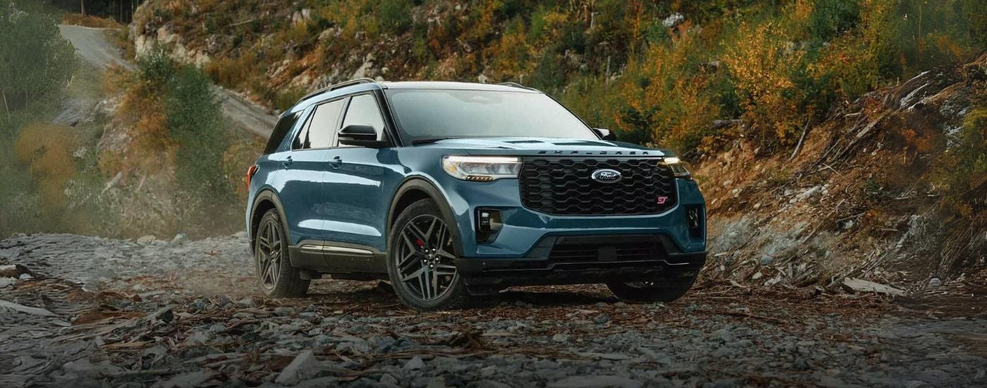 Blue 2025 Ford Explorer parked off-road near a forest.