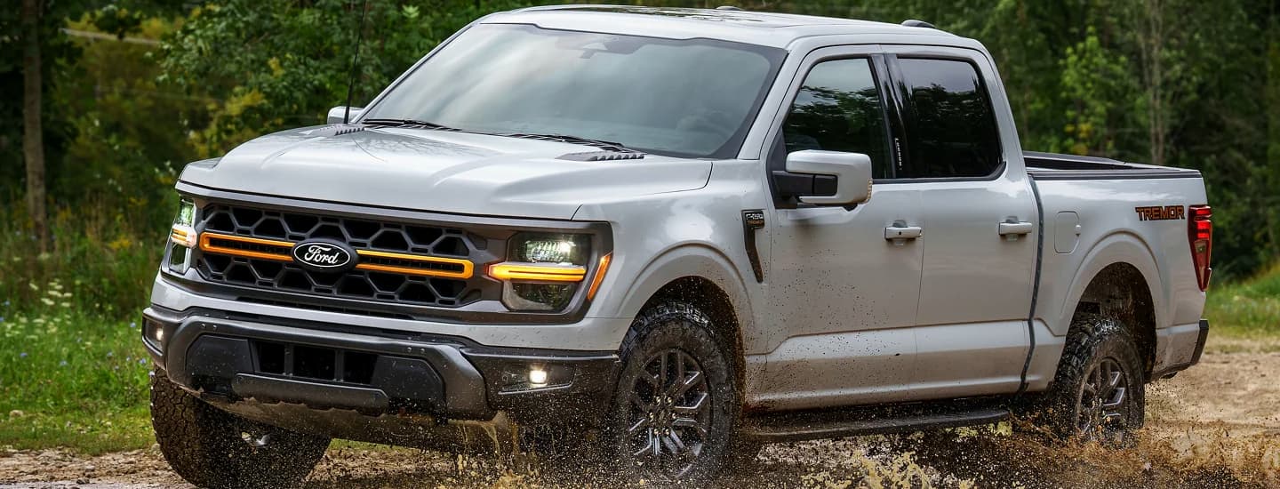 A silver 2026 Ford F-150 driving off-road in mud.